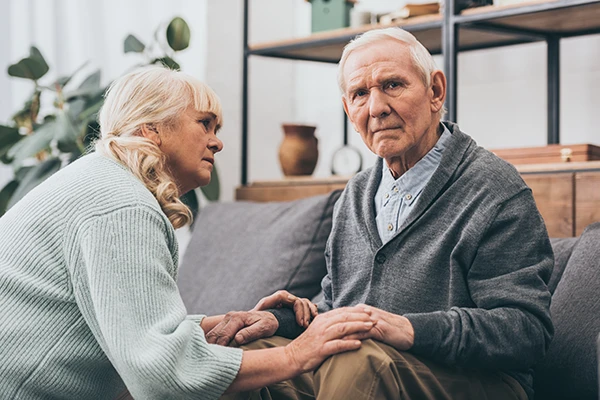 old woman concerned holding hands with old man with Alzheimer's